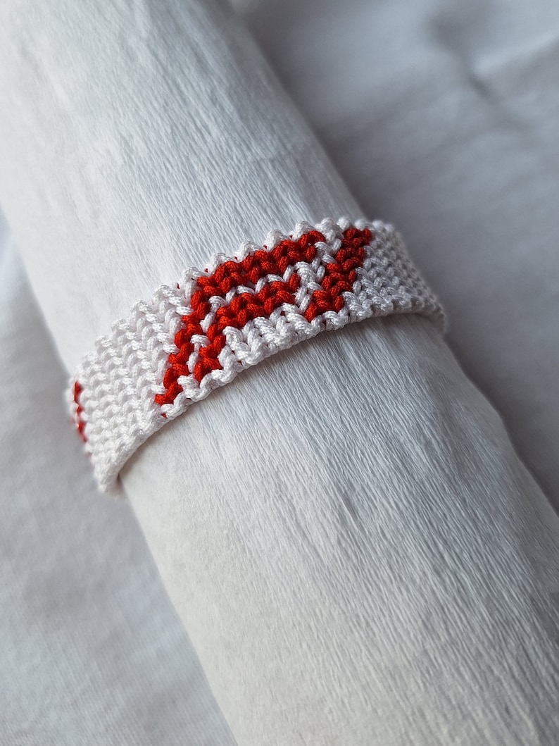 May include: White and red friendship bracelet with a chevron pattern.