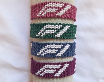 May include: Four woven friendship bracelets arranged vertically. Each bracelet features a white geometric logo pattern against a solid background color: dusty rose, forest green, slate blue, and deep plum. The bands are crafted with a tight knot texture.