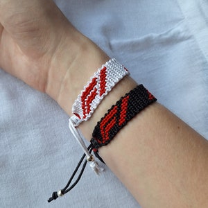 May include: Two friendship bracelets, one white with red stripes and one black with red stripes.