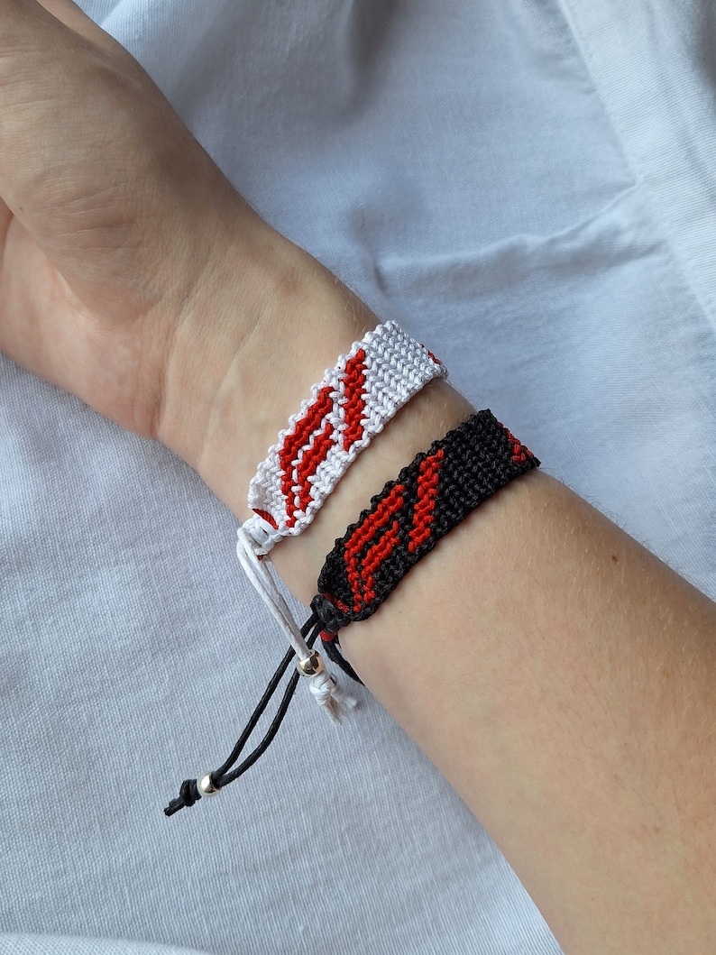 May include: Two friendship bracelets, one white with red stripes and one black with red stripes.