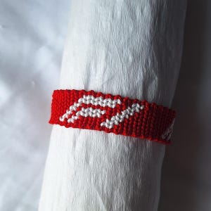May include: Red and white friendship bracelet with a woven pattern.