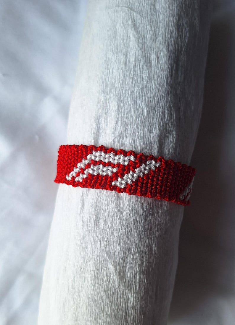 May include: Red and white friendship bracelet with a woven pattern.