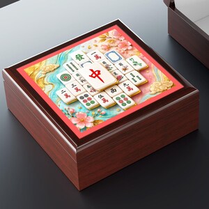 Peut inclure: Une boîte en bois foncé avec un couvercle à charnière ouvert et une seconde boîte assortie fermée. La boîte fermée présente un panneau supérieur carré affichant une illustration colorée de tuiles de Mahjong avec des caractères chinois.