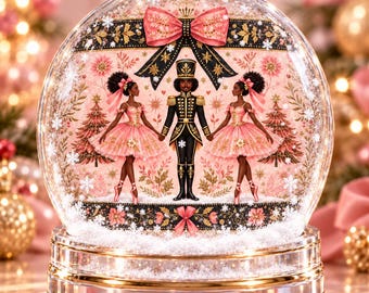 May include: A clear glass snow globe featuring a central nutcracker figure flanked by two ballerinas in pink tutus. The scene includes pink Christmas trees, a large pink bow at the top, and a gold-trimmed base with white snow-like particles inside.
