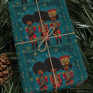 May include: Wrapped gift with teal wrapping paper featuring illustrations of toy soldiers in red and gold uniforms. The gift is tied with twine and set against a backdrop of pine needles and pine cones, evoking a festive holiday theme.