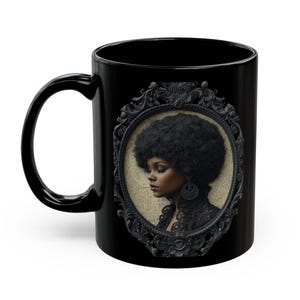 May include: A black ceramic mug featuring a central oval portrait of a person with a large afro hairstyle, wearing dark lace clothing and a circular earring. The portrait is enclosed in an ornate, dark, carved-style decorative frame.
