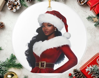 May include: A round Christmas ornament featuring a woman in a Santa Claus outfit. The woman has long black hair and is wearing a red dress with white fur trim and a Santa hat. The ornament has a gold string for hanging.