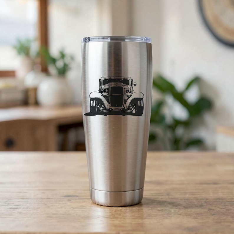 May include: A stainless steel tumbler with a black vintage car graphic. The car is a classic model with large headlights and a detailed front end. The tumbler is cylindrical and has a silver lid.