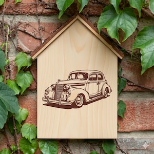 May include: Wooden house-shaped sign with a brown vintage car illustration. The sign is made of light-colored wood with a brown roof trim. The background is a brick wall with green leaves.