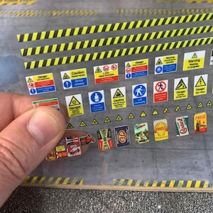 Puede incluir: Una hoja de pegatinas en miniatura con señales de advertencia como "Peligro" y "Precaución", además de logotipos de marcas vintage como "Champion", "STP", "Shell" y "Coca-Cola".
