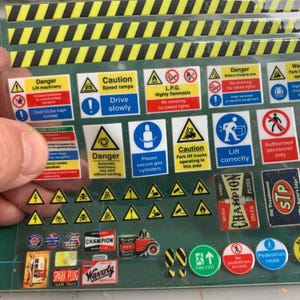 Op de afbeelding: Een vel met diverse veiligheids- en waarschuwingsstickers. De stickers hebben verschillende kleuren, waaronder geel, rood, blauw en wit. De stickers bevatten tekst zoals "Gevaar", "Voorzichtig" en "L.P.G. Zeer ontvlambaar".