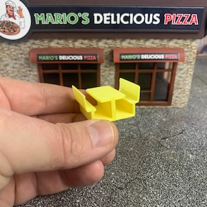 May include: A yellow plastic miniature picnic table with two benches. The table is approximately 5 cm wide and 7.5 cm long.