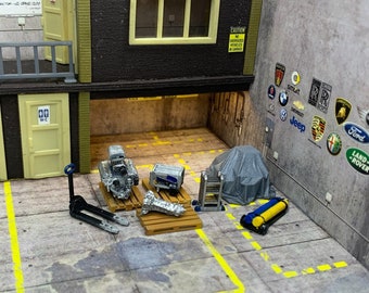 May include: A miniature model of an auto repair shop with a gray tarp, a silver engine, a blue toolbox, a pallet jack, and a blue and yellow gas tank. The shop has a sign that reads "AUTO SERVICE" and a sign that reads "CAUTION NO OVERSIZED VEHICLES IN GARAGE".