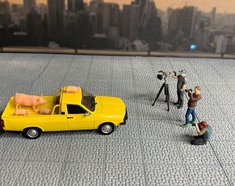 Diorama 1-43 com grandes fotógrafos, incluindo um fotógrafo (homem e mulher) e figuras de pessoas tirando fotos de carros com câmeras.