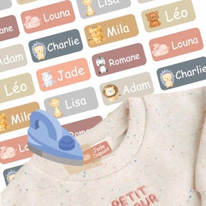 May include: A collection of personalized name labels in various pastel colors, each featuring a different animal illustration. The labels are being applied to a light-colored garment with a blue iron. The labels have names like "Louna", "Charlie", and "Jade".