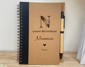 May include: A brown spiral notebook with a black spine and a matching pen. The cover features a floral design with the letter "N" and the text "comme Merveilleuse Nounou Jeanne".