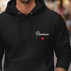 Puede incluir: Sudadera con capucha negra con bolsillo delantero y cord&oacute;n. La palabra "Parrain" est&aacute; escrita en cursiva, con un peque&ntilde;o coraz&oacute;n rojo debajo. La sudadera es de color negro liso.