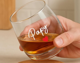 May include: A clear glass tumbler filled with amber liquid, featuring the word "Papy" in white script and a small red heart. The glass rests on a cork coaster. The image is of a drinkware item.