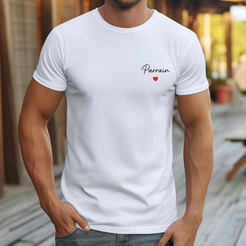 Puede incluir: Camiseta blanca con la palabra "Parrain" en escritura negra y un peque&ntilde;o coraz&oacute;n rojo. La camiseta est&aacute; hecha de un material suave y tiene mangas cortas. Es una prenda informal.