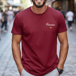 Puede incluir: Una camiseta granate con la palabra "Parrain" en escritura cursiva y un peque&ntilde;o coraz&oacute;n dorado. La camiseta es de manga corta y parece estar hecha de un material suave.