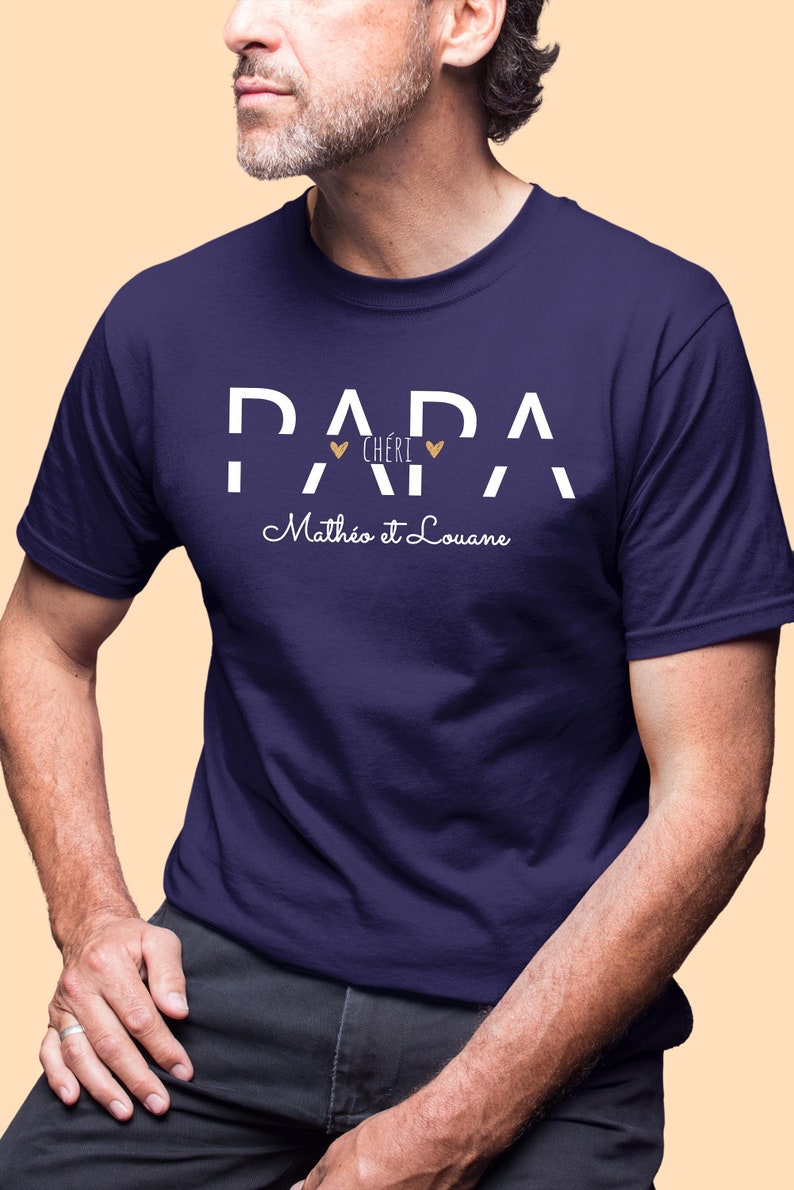 Pode incluir: Uma camiseta azul marinho com texto branco que diz "Papa Cheri" com dois pequenos cora&ccedil;&otilde;es dourados e "Matheo et Louane" em letra cursiva.