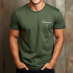 Puede incluir: Camiseta verde oliva con la palabra "Parrain" en escritura cursiva y un peque&ntilde;o coraz&oacute;n. La camiseta tiene cuello redondo y mangas cortas.