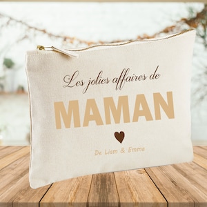 Peut inclure: Une pochette zippée en toile blanche avec le texte "Les jolies affaires de MAMAN" en lettres brunes. Le texte "De Liam & Emma" est imprimé sous le texte principal en lettres brunes avec un petit symbole de cœur brun.
