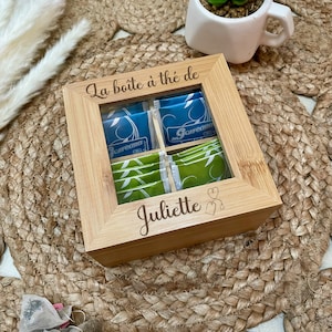 May include: A wooden tea box with a glass window showing tea bags. The box is engraved with the text "La boîte à thé de Juliette" and a teacup icon.