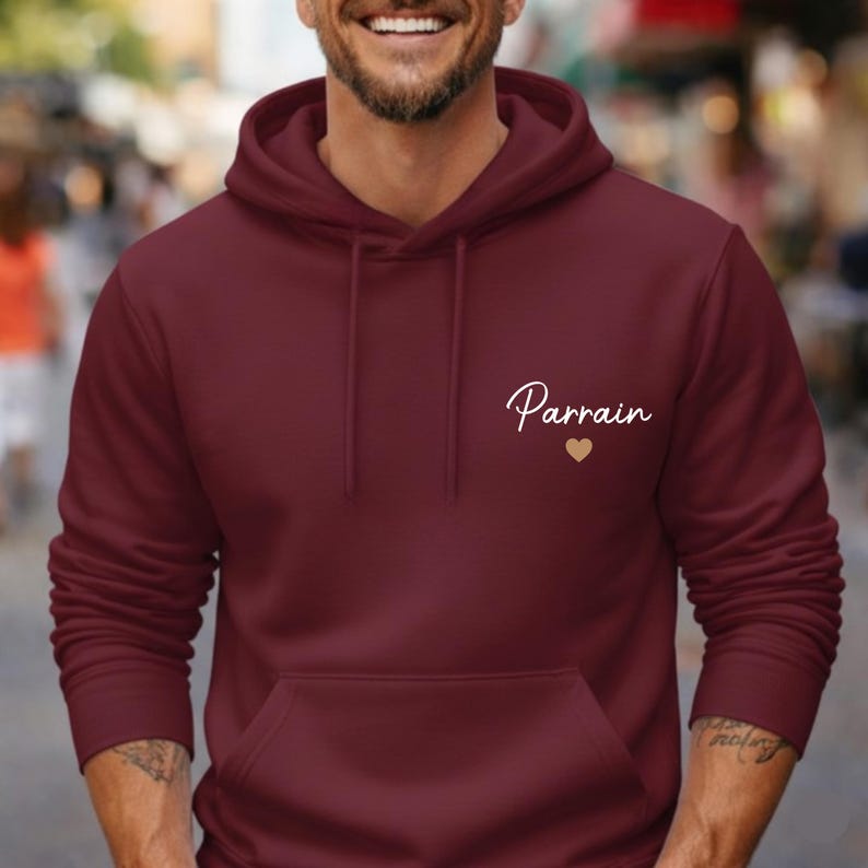 Puede incluir: Una sudadera con capucha burdeos con un bolsillo delantero y una capucha con cord&oacute;n. La palabra "Parrain" est&aacute; escrita en cursiva en el pecho, acompa&ntilde;ada de un peque&ntilde;o coraz&oacute;n dorado.
