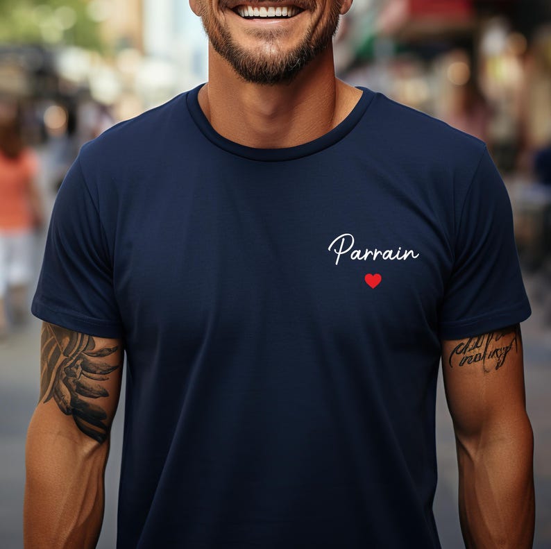 Puede incluir: Camiseta azul marino con la palabra "Parrain" en cursiva y un peque&ntilde;o coraz&oacute;n rojo. La camiseta tiene mangas cortas y cuello redondo.