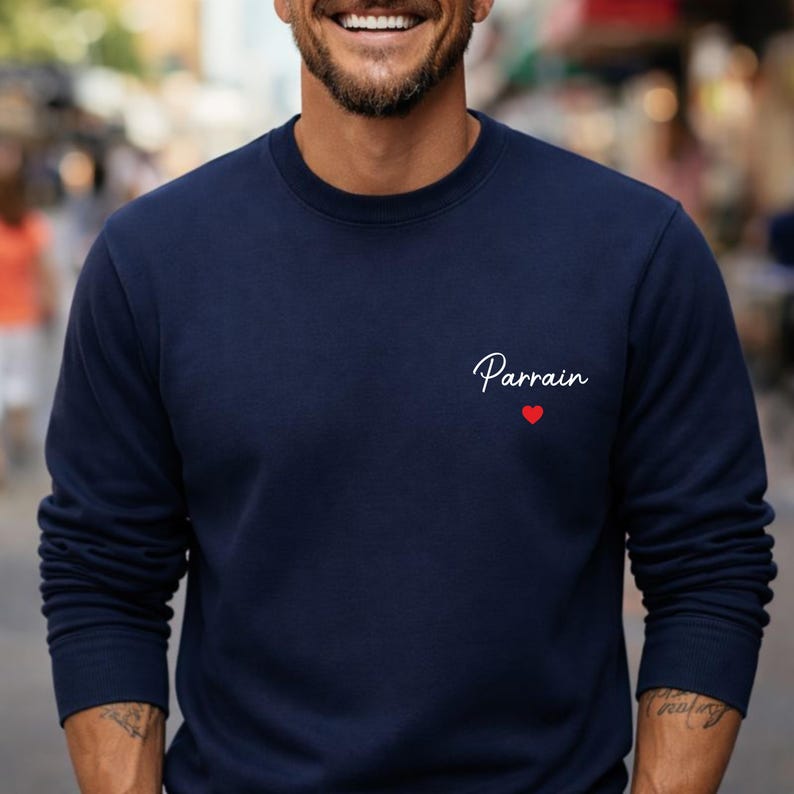 Puede incluir: Sudadera azul marino con la palabra "Parrain" en escritura blanca y un peque&ntilde;o coraz&oacute;n rojo. La sudadera de cuello redondo es de color liso y tiene mangas largas.