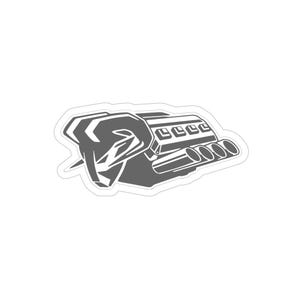 Puede incluir: Una pegatina gris que presenta una ilustración estilizada de un motor. El diseño incluye el bloque del motor, los tubos de escape y otros componentes mecánicos. La pegatina tiene un borde blanco.