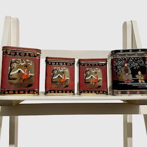 May include: A set of four rectangular metal storage tins featuring decorative panels with illustrations of figures in traditional attire, cherry blossom trees, and mountain landscapes, accented with black, red, and gold geometric border patterns.