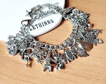 May include: Silver charm bracelet with various detailed charms, including an Eiffel Tower, an astronaut, and a bee. The bracelet is on a white surface with the word "LETHINNS" printed on it. The bracelet has a lobster clasp.
