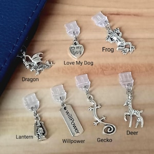 May include: A collection of silver-toned charms, each with a clear plastic clip. The charms include a dragon, a frog, a deer, a lantern, a gecko, and a heart-shaped charm with the words "Love My Dog". Another charm reads "Willpower".