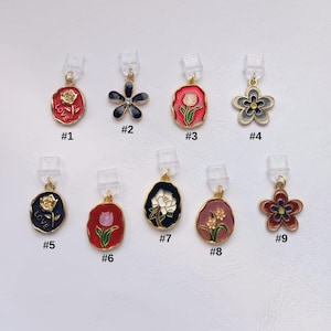 Puede incluir: Una colección de nueve colgantes decorativos con diseños florales y abstractos. Cada colgante presenta una combinación de colores diferente, incluyendo rojo, negro y dorado. Algunos colgantes tienen la palabra "LOVE". Los colgantes están unidos a clips de plástico transparente.