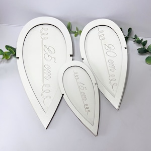 Puede incluir: Tres bandejas de madera blanca en forma de hoja con medidas grabadas: 25 cm, 20 cm y 15 cm.