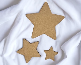 May include: Three wooden stars of different sizes on a white fabric background. The largest star is in the centre, with a smaller star to the left and the smallest star to the right.