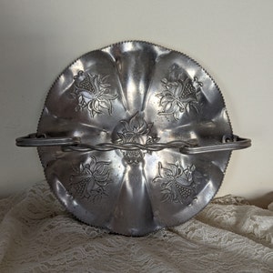 May include: A silver metal serving tray with a decorative floral design and a twisted wire handle. The tray has a scalloped edge and is perfect for serving snacks or appetizers.