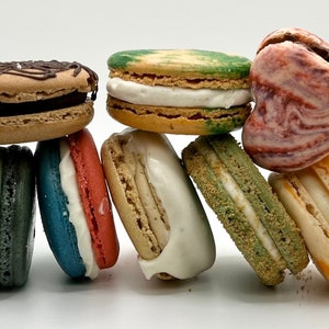 May include: A collection of eight colorful macarons, some with white filling, stacked on top of each other. The macarons are arranged in a row, with the largest macaron on the bottom and the smallest macaron on top.