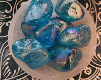 May include: A collection of iridescent blue tumbled stones in a white bowl. The stones have a shimmering, almost holographic effect.