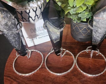 May include: Three silver hoop earrings with rhinestones displayed on black crystal stands. The stands are on a wooden surface.