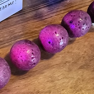 May include: Five purple lava rock spheres with a textured surface. The spheres are arranged in a row on a wooden surface.