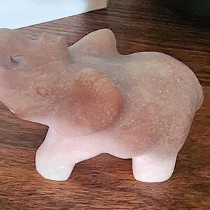 May include: A small, pink, carved stone elephant figurine. The elephant is standing on all four legs with its trunk raised in the air.