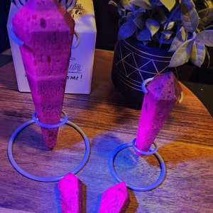 May include: Four pink crystal points on metal stands. The crystals are on a wooden surface. The crystals are glowing under a black light.