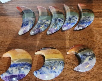 May include: Seven rainbow moonstone crescent shaped crystal healing stones. Each stone is layered with seven different colors, including red, orange, yellow, green, blue, indigo, and violet.