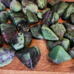 May include: A collection of green, black, and pink tumbled stones. The stones are smooth and have a variety of shapes and sizes.