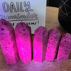 May include: Six pink, faceted, crystal-like points, with a rough, textured surface. The points are arranged in a row, with the largest point on the left and the smallest point on the right.