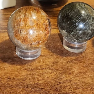 May include: Four polished gemstone spheres on display stands. The spheres are various shades of green, brown, and black.