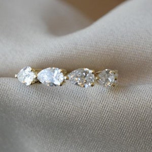 May include: A gold band ring with five pear-shaped clear gemstones set in a row.